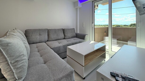 Ein modernes Wohnzimmer mit einem grauen Ecksofa, einem weißen Couchtisch und einem Fernseher auf einem Lowboard.