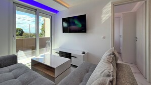 Ein modernes Wohnzimmer mit einem an der Wand befestigten Flachbildfernseher, einer Glastür zum Balkon und einem Sofa.