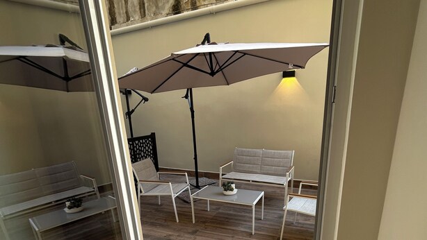 A glass-enclosed patio with wooden flooring, two white tables, and two chairs. - Somnia Luxury Rooms  (Naples)