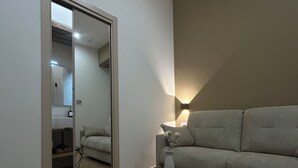 A modern living room with a sofa, a coffee table, and a lamp. There is a mirror on the wall and an air conditioning unit above it. - Somnia Luxury Rooms  (Naples)