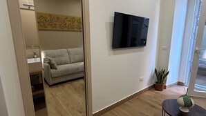 A modern living room with a sofa, a TV mounted on the wall, and a small table with a decorative item. - Somnia Luxury Rooms  (Naples)