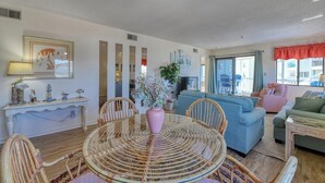 Ein geräumiges Wohnzimmer mit einem runden Glastisch, Korbstühlen, einem blauen Sofa und einer rosa Vase mit Blumen.
