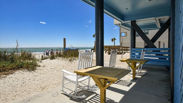 Eine Terrasse am Strand mit Holztischen und weißen Stühlen, mit Blick auf den Ozean.