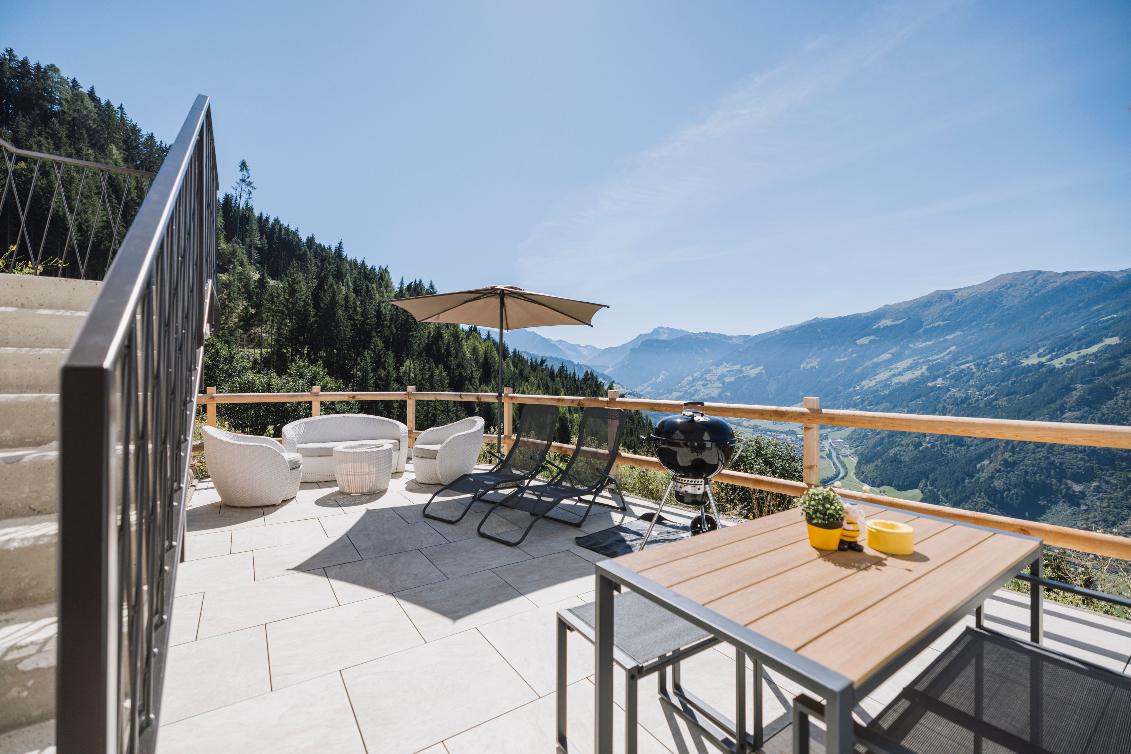 A terrace with outdoor furniture, a grill, and a view of mountains.