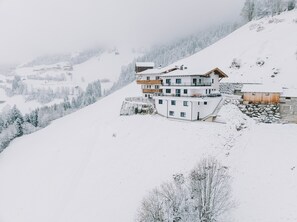 A multi-story building with a modern design, situated on a snow-covered slope with a view of a forested valley. - Apartment 'Persal' with Mountain View, Private Terrace and Wi-Fi (Rohrberg)