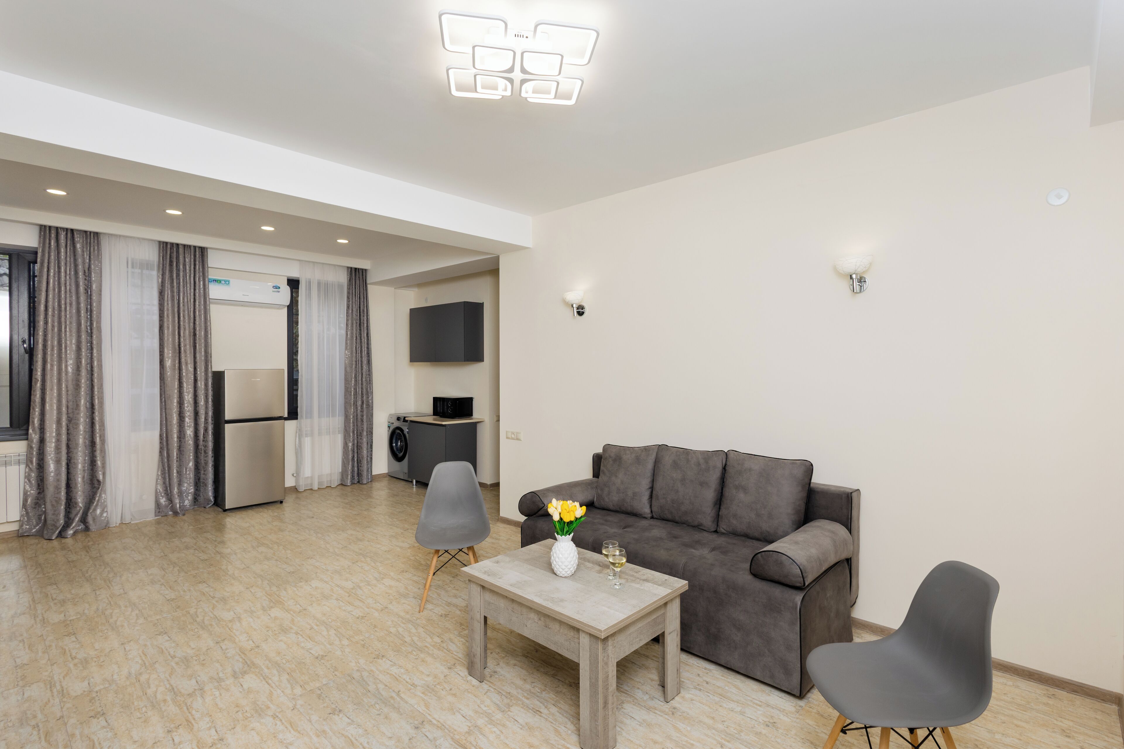 A modern living room with a grey sofa, a small table with a vase and a glass, and a grey armchair.