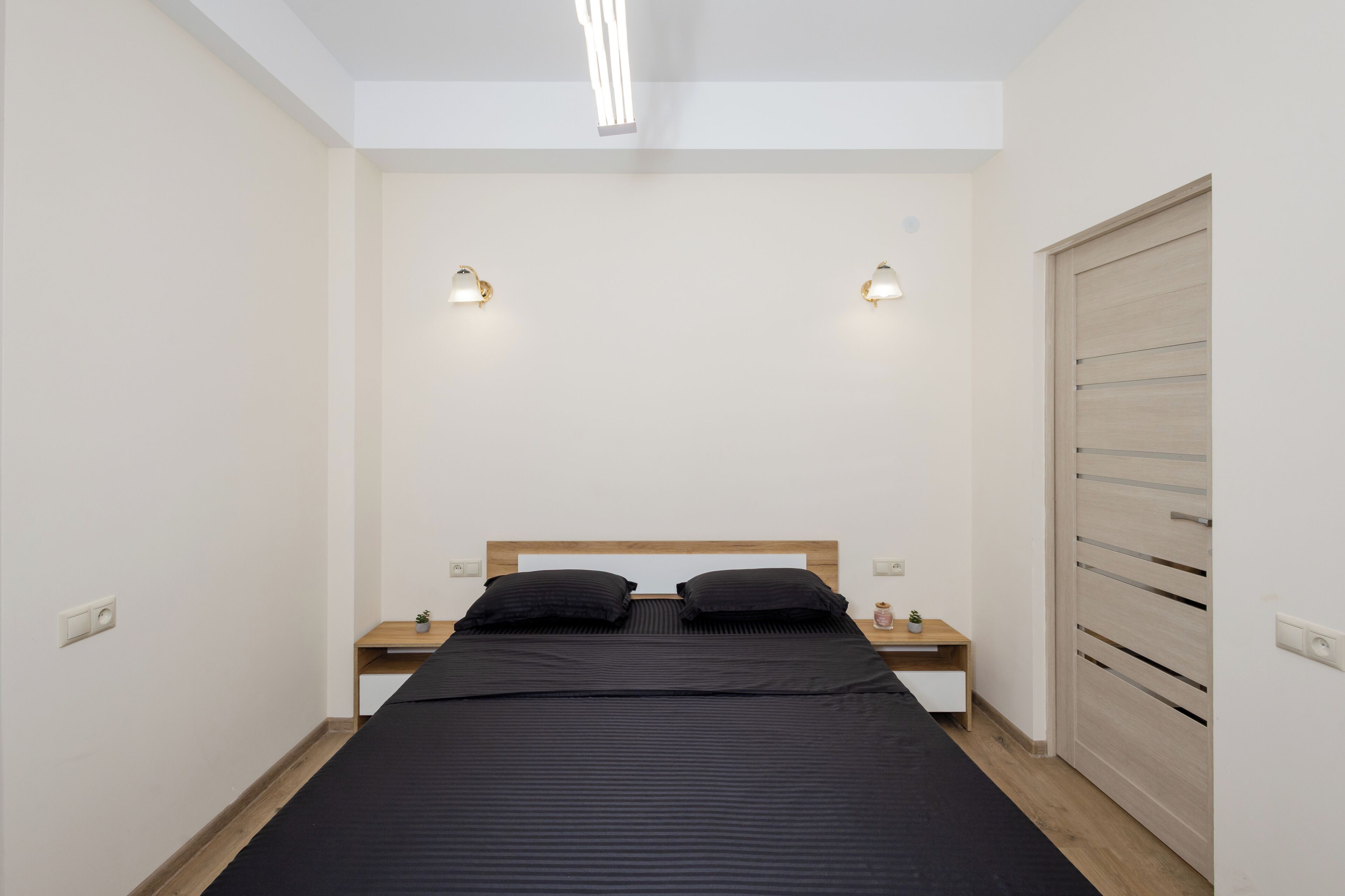 Een slaapkamer met een bed, nachtkastjes, een kledingkast van hout en wandlampen.