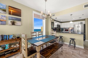 Une cuisine moderne avec vue sur l’océan, un coin repas avec une table et des chaises en bois, et une bibliothèque contenant des livres et des objets décoratifs.