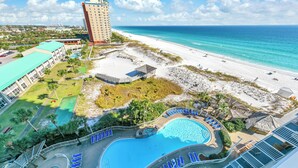 Ein Resort mit großem Pool, Zugang zum Strand und einem hohen Gebäude im Hintergrund.