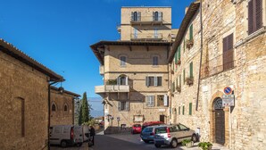 A narrow street with stone buildings, parked cars, and a no parking sign.