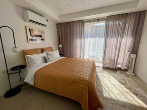 Une chambre d’hôtel avec un lit, une lampe sur pied, un tableau au mur et une fenêtre avec des rideaux.