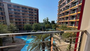 Un balcón con una mesa y sillas de vidrio que da a una piscina y edificios cercanos.