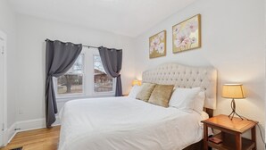 Um quarto bem organizado com uma cama grande, uma mesa de cabeceira com abajur e duas pinturas florais na parede.