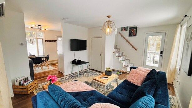A modern living room with a blue sofa, a coffee table, and a TV. There is a staircase leading to another level, and a door with a window.