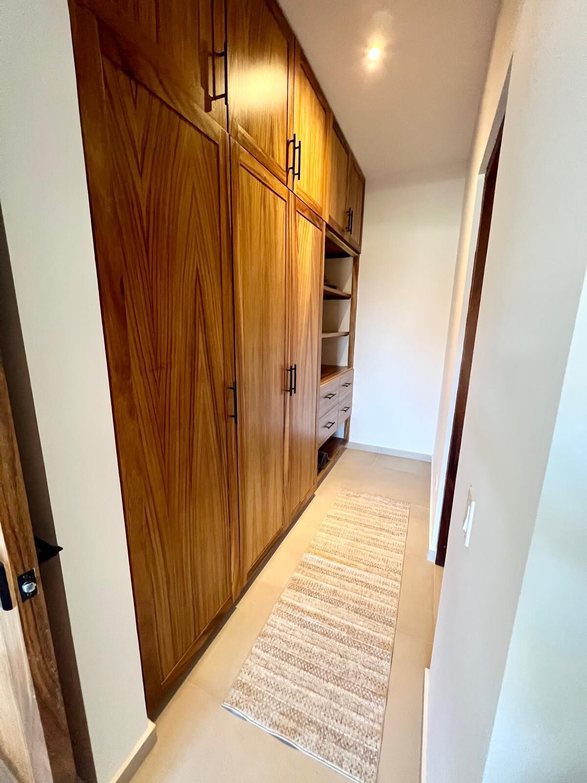 Un couloir avec des armoires en bois, un tapis à motifs et un mur blanc.