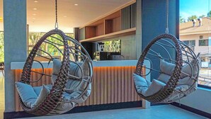 Two wicker hanging chairs with cushions in a modern lobby area with a reception desk and a view of the outside. - Fresh Triple Double | Free Breakfast, Spa & 5 mi to Three Borders (Paraná)