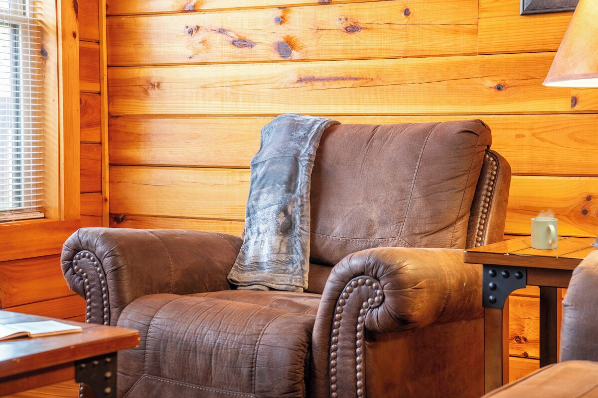 A leather armchair with a blanket, a wooden table with a mug, and a wooden wall.