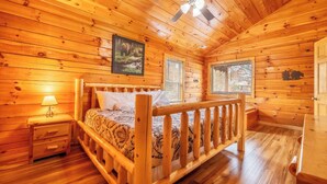 A wooden cabin bedroom with a bed, a nightstand, a ceiling fan, and two windows. - *2BD w/ POOL Access Near TOWN! Theater + Hot Tub* (Pigeon Forge)
