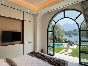 Ein modernes Hotelzimmer mit einem großen Bogenfenster, das einen Blick auf einen See und Berge bietet.