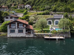Ein Steinhaus mit rotem Dach an einem See, mit Schwimmbad und Steg.