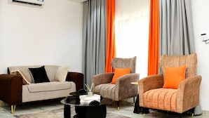 Uma sala de estar moderna com um sofá, duas poltronas, uma mesa de centro e uma janela grande com cortinas.