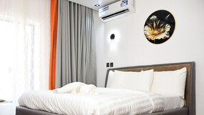 Cama bem arrumada com lençóis brancos e toalha dobrada, cabeceira estofada cinza e ar-condicionado fixado na parede.