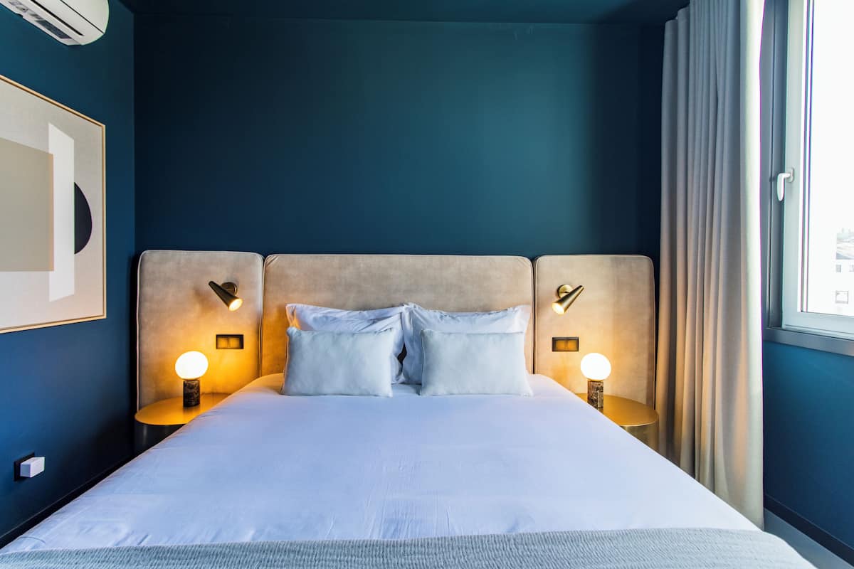 Una cama bien hecha con dos almohadas, un cabecero con iluminación integrada y una mesita de noche con lámpara.