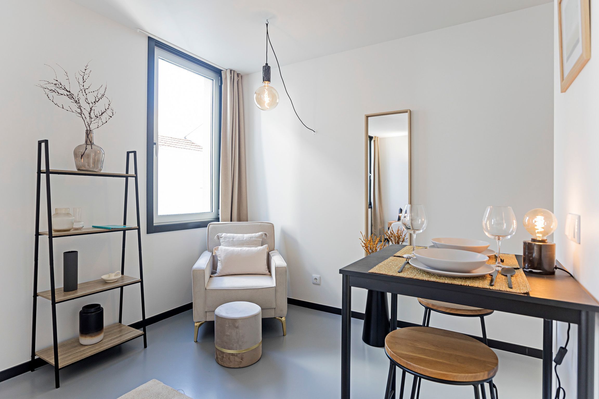 Uma área de refeições moderna com uma cadeira minimalista, uma mesa de jantar com pratos e copos, e uma luminária pendente.