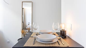 Una mesa de comedor dispuesta con platos, cubiertos y copas de vino, con una lámpara y un espejo al fondo.