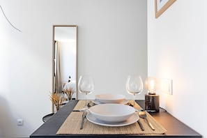 A dining table set with plates, cutlery, and wine glasses, with a lamp and a mirror in the background.