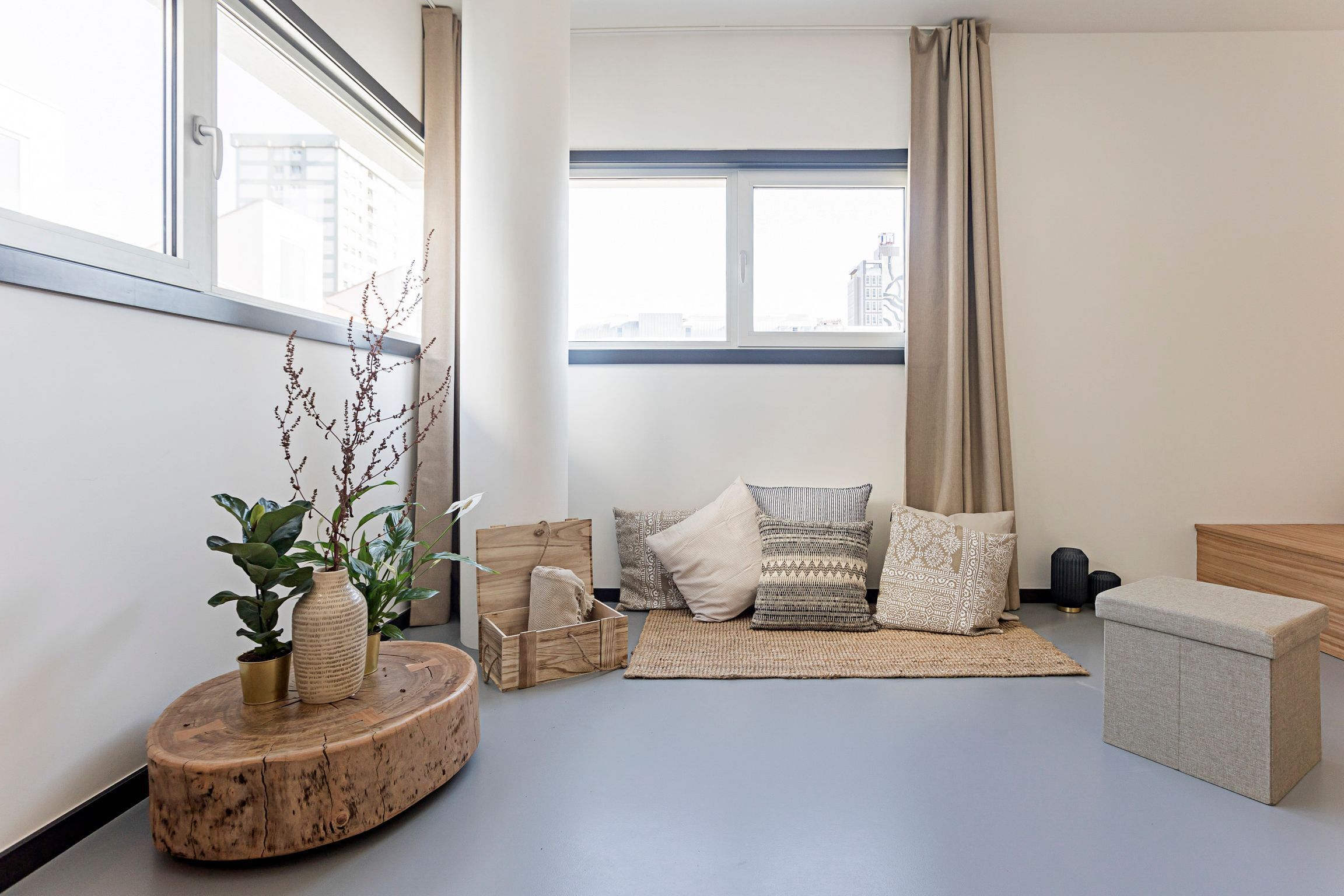 Una sala moderna con un ventanal grande, una mesa de centro de madera, un sofá con cojines estampados y un pequeño otoman.