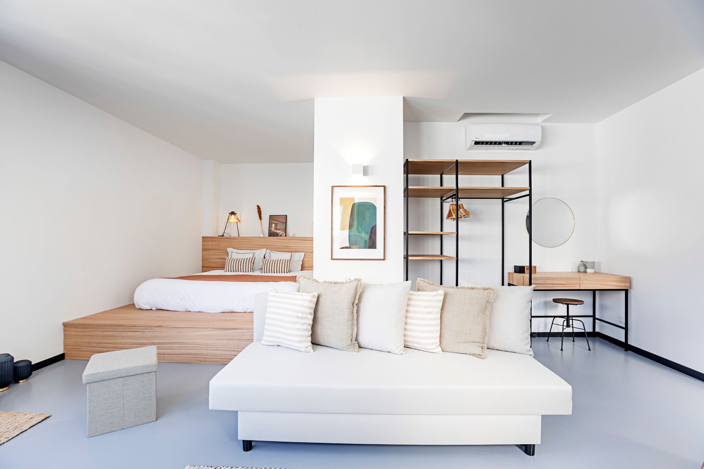 A modern bedroom with a bed, a white sofa, a desk, and a shelving unit.