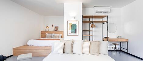 A modern bedroom with a bed, a white sofa, a desk, and a shelving unit.
