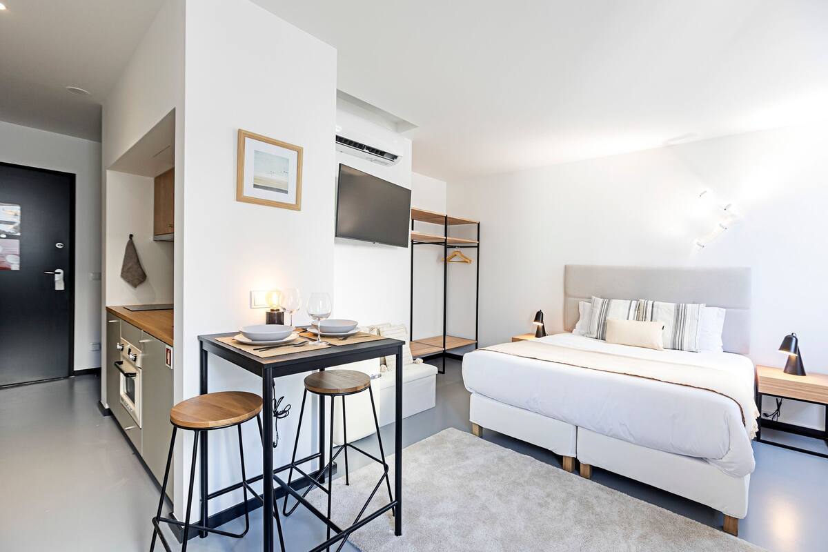 Un dormitorio moderno con cama, mesita de noche y escritorio con taburetes.