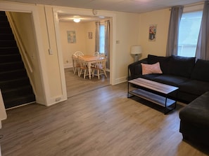 Una sala de estar con un sofá oscuro, una mesa de centro y un comedor con una mesa y sillas.