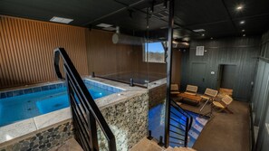 Une piscine bordée d’un mur en pierre, avec un revêtement en bois et un espace jacuzzi fermé par des parois de verre.