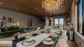 A spacious living area with a long dining table set for a meal, a cozy seating arrangement, and a large chandelier. - Rooftop Deck w Fireplace, Pool w/ Grotto, Game Room, Hot Tub, Panoramic Views (Sevierville)