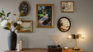 En vägg med inramade konstverk, en vas med blommor, en skivspelare och en lampa.