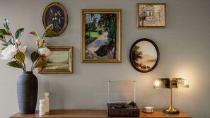 Eine Wand mit gerahmten Kunstwerken, einer Blumenvase, einem Plattenspieler und einer Lampe.