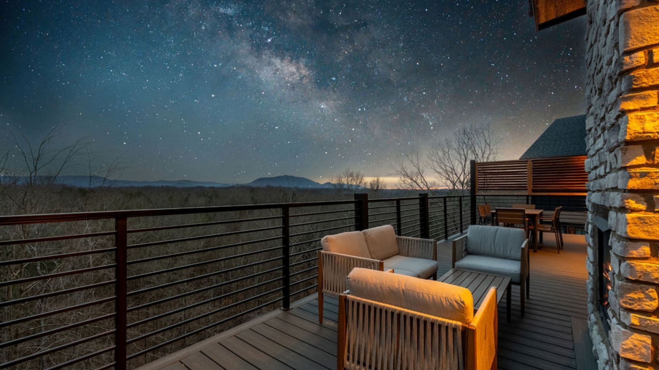 A deck with outdoor furniture, a stone wall, and a night sky with stars.