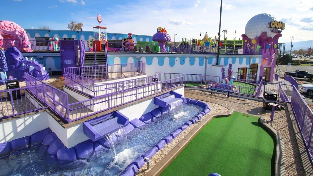 Parque acuático interior con una zona de juegos de color morado, una sección de césped verde y una gran atracción esférica.