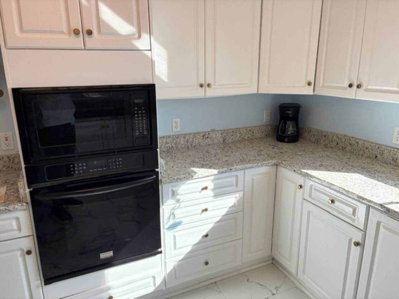 A kitchen with white cabinets, a black microwave, and a coffee maker.