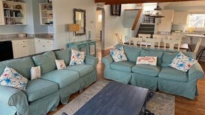 Ein großzügiger Wohnbereich mit zwei hellblauen Sofas, einem dunkelholztischen Couchtisch und einer Küche im Hintergrund.