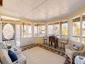 A sunroom with a view of the neighborhood, wicker furniture, and a decorative mirror. - Corolla Coastal Oasis 
Location, Amenities & Vibes (Currituck County)