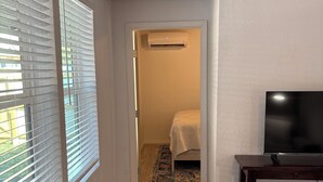 A hallway with a ceiling fan, a bed with a patterned bedspread, a television on a stand, and a wooden floor. - Delightful, easy living, 1-bedroom apartment with AC in San Antonio (San Antonio)