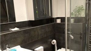 A modern bathroom with a glass shower enclosure, a white sink, a toilet, and a dark-toned vanity with cabinets.