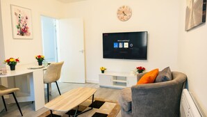 A modern living room with a flat-screen TV, a dining area with a table and chairs, and a sofa with cushions. - Cozy 2BR Flat Near Cardiff City Centre | Stadium| Shops | Uni (Cardiff)