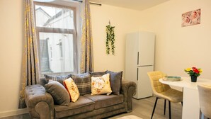 A cozy living room with a sofa, a dining table, and a refrigerator. - Cozy 2BR Flat Near Cardiff City Centre | Stadium| Shops | Uni (Cardiff)
