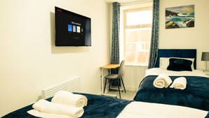 A hotel room with two beds, a desk, a chair, a TV displaying a Netflix interface, and a painting on the wall. - Cozy 2BR Flat Near Cardiff City Centre | Stadium| Shops | Uni (Cardiff)