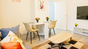 A modern living room with a sofa, a coffee table, and a dining area with chairs and a small table. There is a TV mounted on the wall and a door leading to another room. - Cozy 2BR Flat Near Cardiff City Centre | Stadium| Shops | Uni (Cardiff)